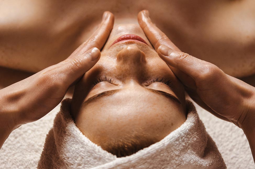 Femme allongée les yeux fermés recevant un massage du visage dans un espace bien-être.