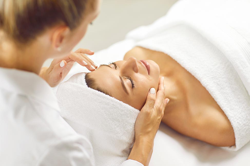 Femme allongée les yeux fermés recevant un soin du visage dans un espace spa.