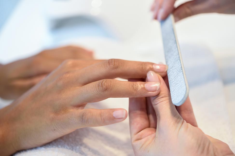 Gros plan sur une manucure avec une professionnelle limant les ongles d’une cliente.